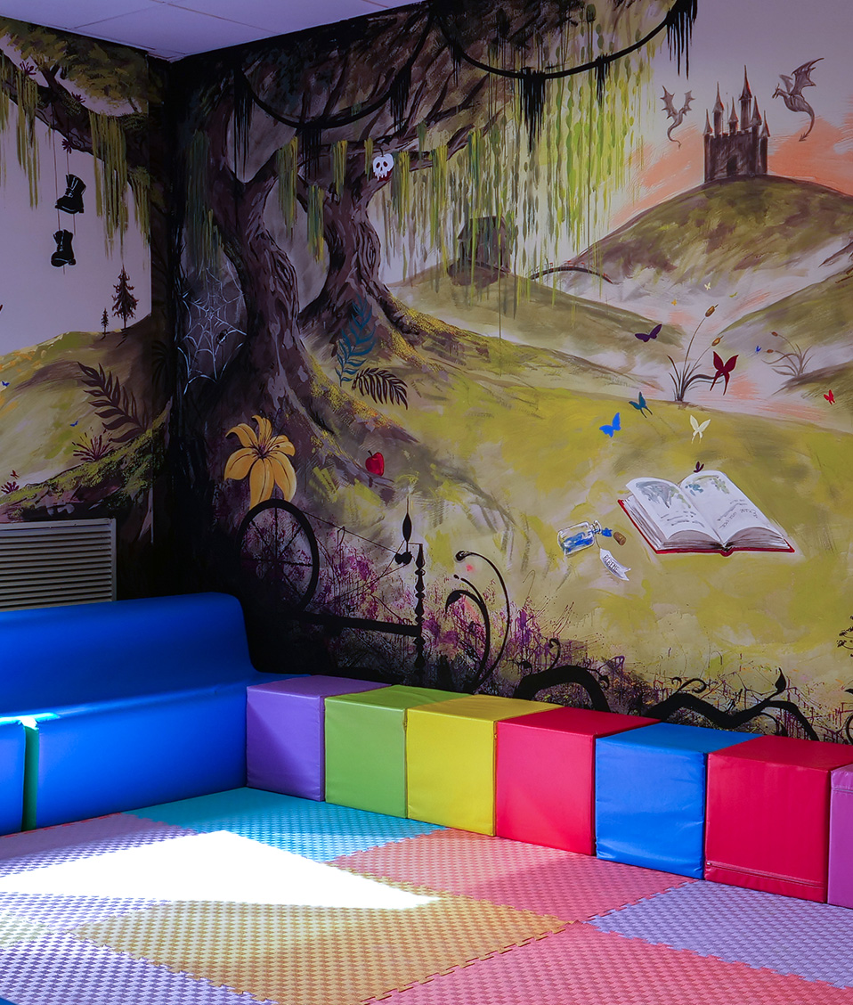 Mural en sala de lectura infantil con mobiliario de colores 